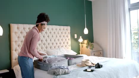 Biracial-woman-packing-suitcase-in-sunny-bedroom,-slow-motion