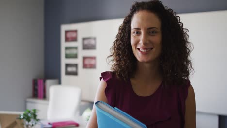 Video-of-happy-caucasian-female-teacher-standing-in-classroom-and-holding-book