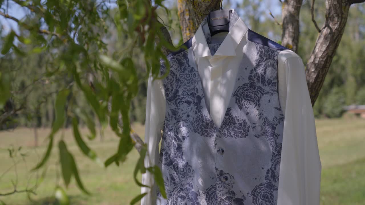 White waistcoat with subtle floral pattern hanging on a tree at wedding venue