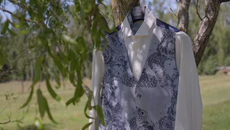 white waistcoat with subtle floral pattern hanging on a tree at wedding venue