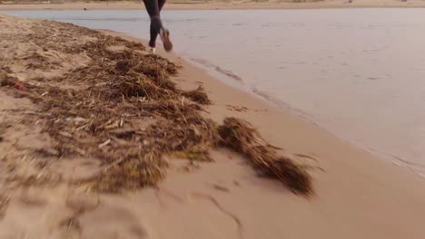 Low-angle-tracking-shot-of-a-female-jogger-on-a-beach-by-the-sea