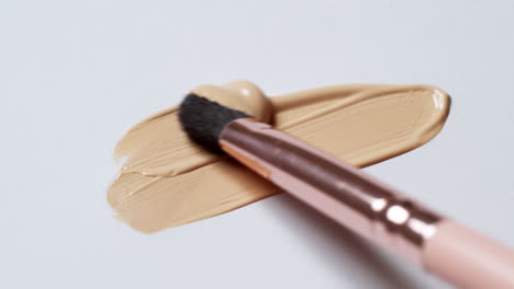 Brushing-a-layer-of-make-up-foundation-on-a-clean,-white-palette-board-to-check-its-texture-and-tone