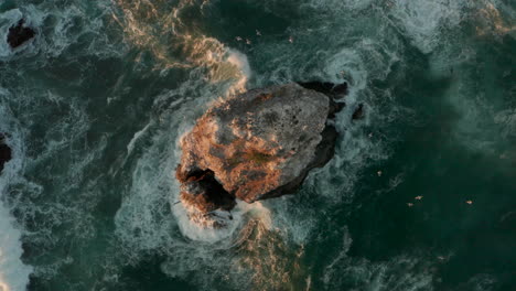 Top-down-aerial-shot-of-waves-crashing-against-a-sea-stack