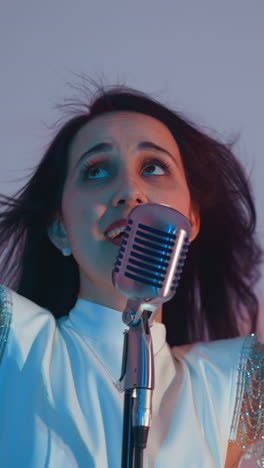 cantante alegre en un vestido blanco actuando con un micrófono vintage, expresando emoción con los ojos cerrados y las manos hacia arriba. en un fondo de luz azul suave y rosa