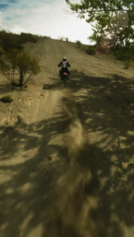 motorcyclist rides uphill in dust cloud fpv drone. professional racer in uniform competes for leadership in extreme racing. motocross route at highland