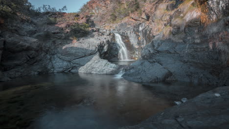 Serenity-at-a-secluded-waterfall-with-glistening-waters,-surrounded-by-rugged-rocks-at-dusk,-long-exposure