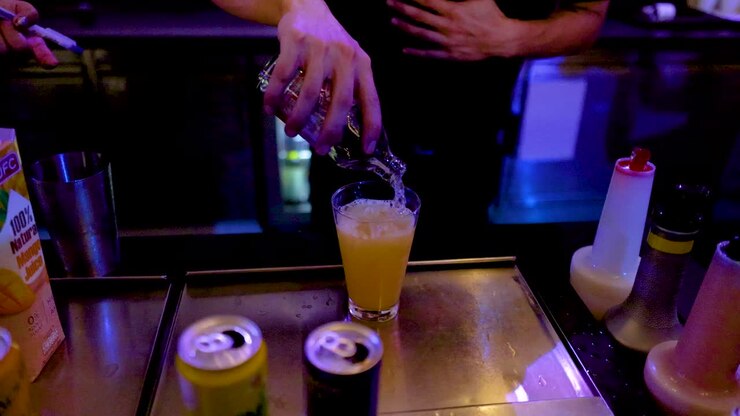 Un barista versa della soda in un cocktail all'arancia con ghiaccio, illuminazione al neon, vista dall'alto, bar di Bangkok