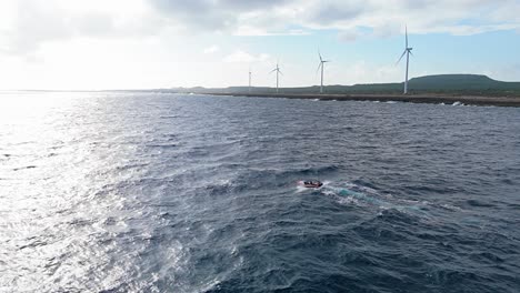 fishermen brave rocky seas in small boat off northside of playa kanoa in curacao with windmill turbines