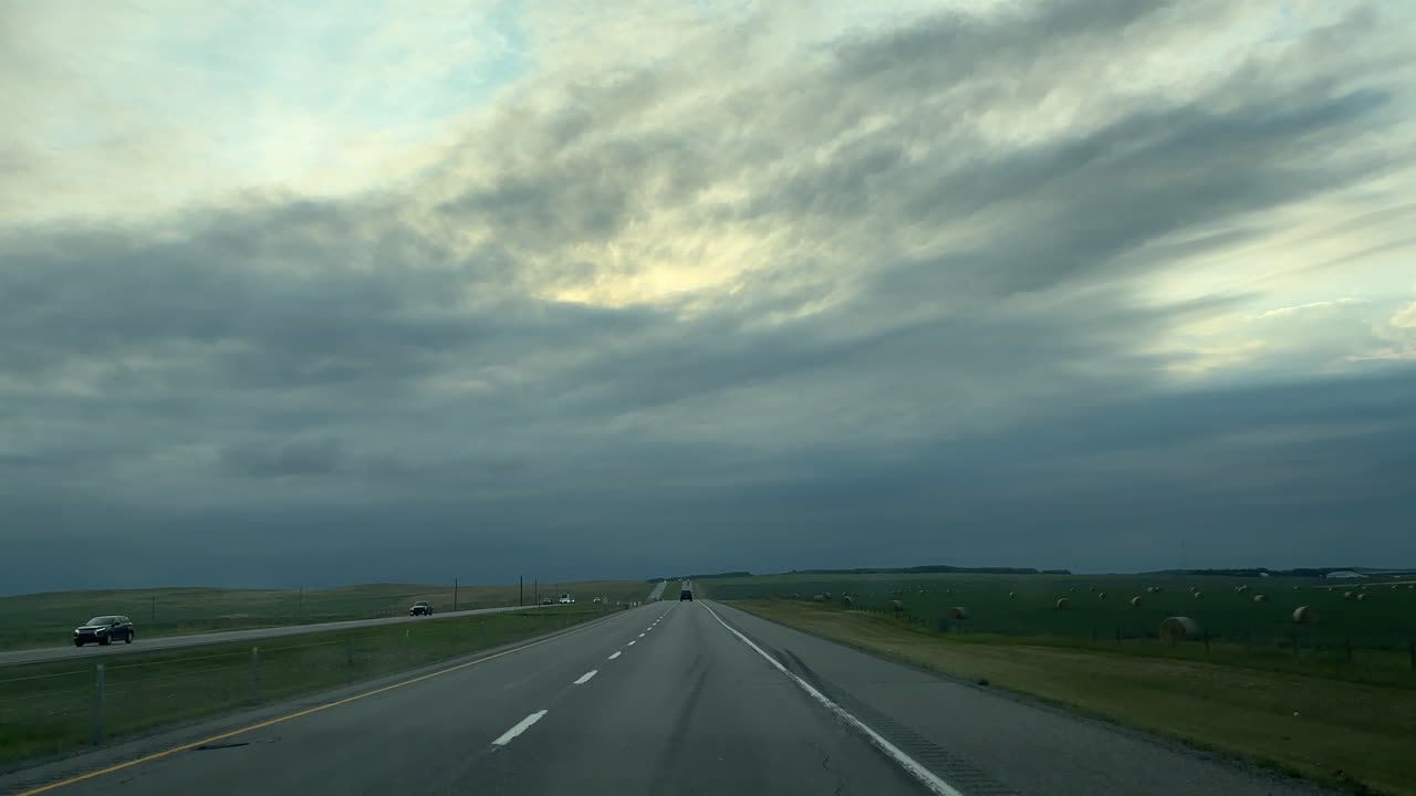 Car Driving On Highway Through Rural Fields With Cloudy Sunset Sky In Banff, Alberta, Canada. wide POV shot