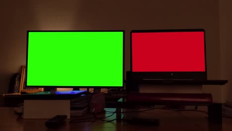 smart tv with green screen near a  laptop with red screen inside a dark room. zoom in. 4k resolution.