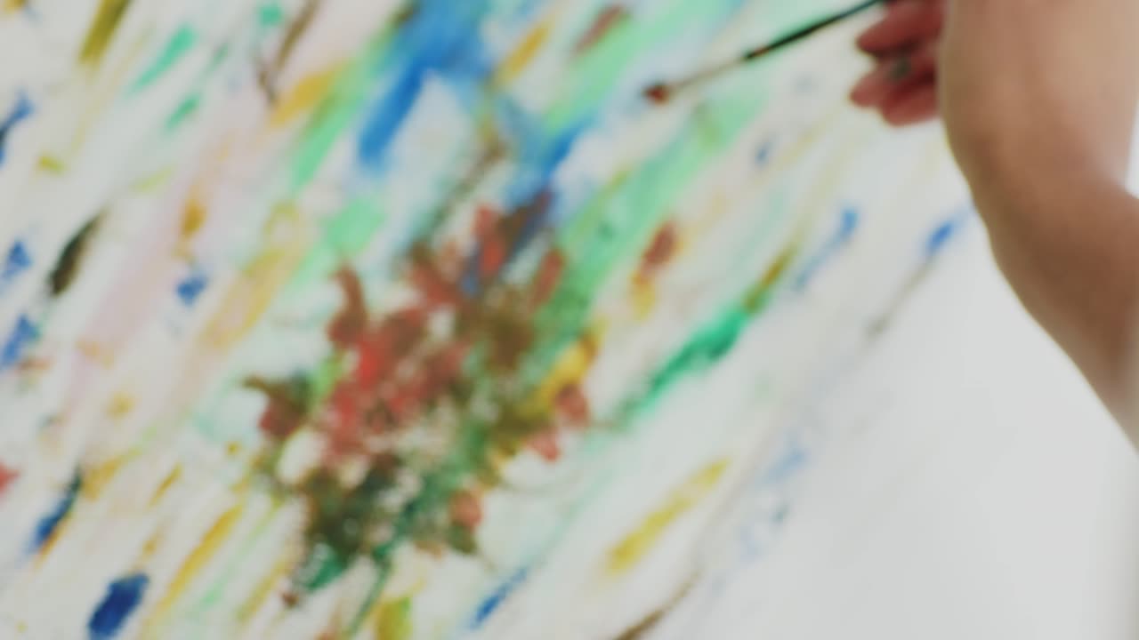 Artist's hands are dipping brush into red paint mixing colors and building floral cluster on canvas