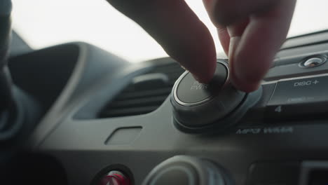 close up hand turning music knob and pressing button on car audio control panel knob interaction with dashboard stereo unit inside vehicle cabin under natural daylight with subtle reflections