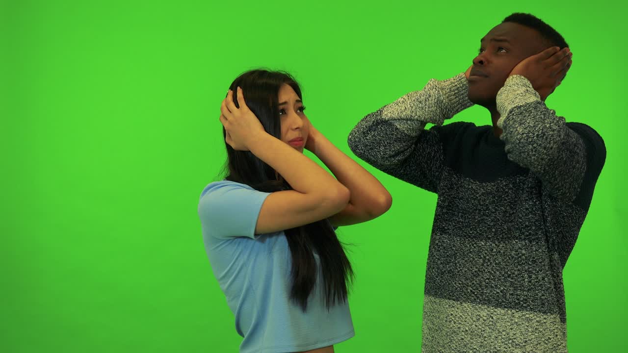 Una giovane donna asiatica e un giovane uomo di colore si coprono le orecchie per un suono sgradevole - studio con schermo verde