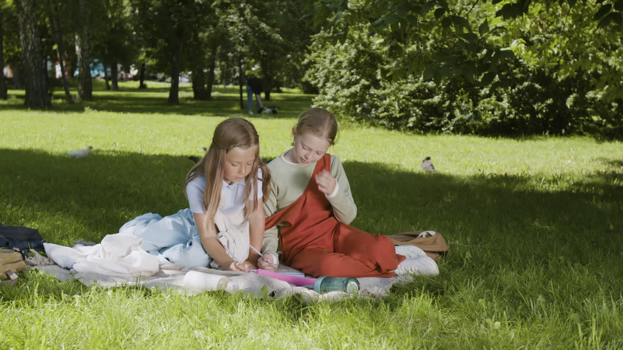 Two happy girls drawing and playing together in a park