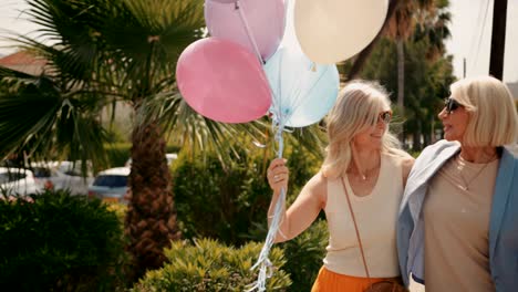 mujeres mayores alegres sosteniendo globos y caminando por la ciudad