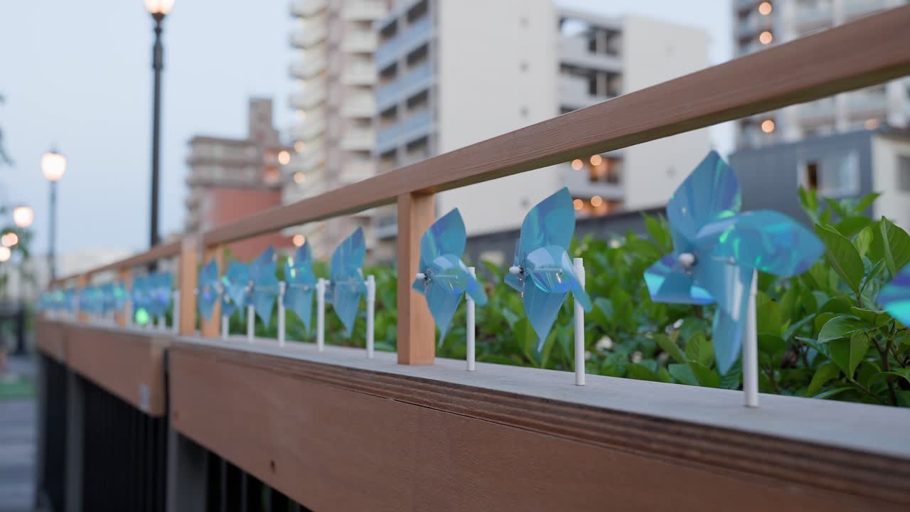 A shot capturing blue pinwheels decorating the railing of the promenade at Tokyo Mizumachi along the Kita-jūkken-gawa River at dusk