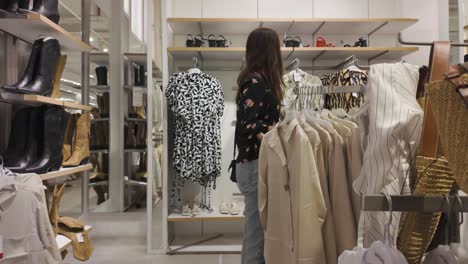 woman shopping for clothes at a trendy boutique, rearview following through store at low angle