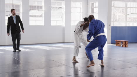 judo practitioners sparring in dojo while instructor observes their technique