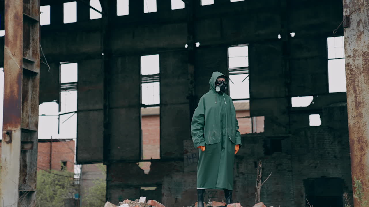 Ecologist in safety suit on ruined building background. Person in gas mask and protective clothes stands in dangerous place after chemical attack.