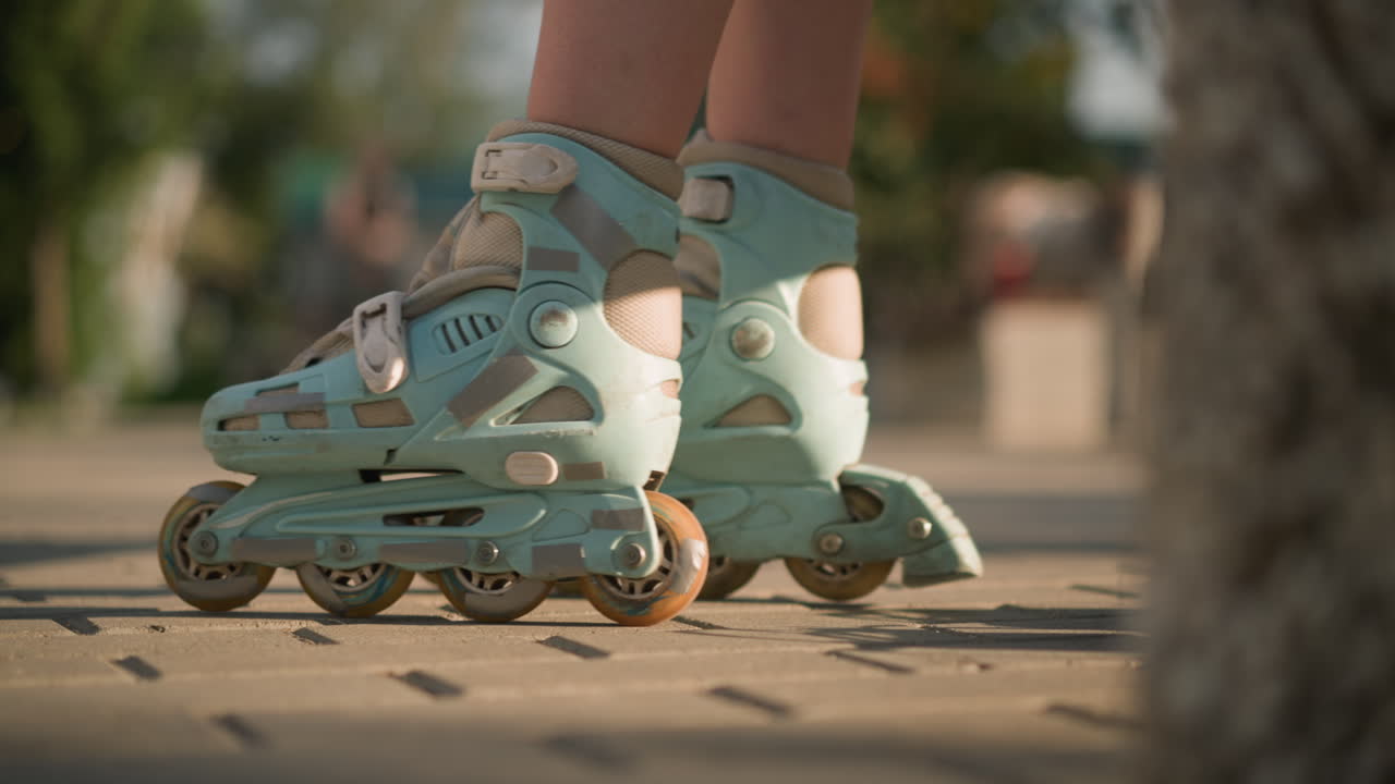 Close-up leg view of individual roller skating on interlocked ground, rolling forward and backward with sun reflecting off skates, with background blurred