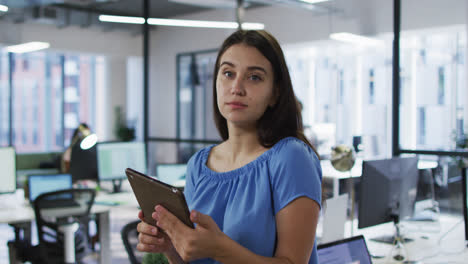 Porträt-Einer-Kaukasischen-Geschäftsfrau,-Die-Im-Büro-Steht-Und-Ein-Tablet-Hält-Und-In-Die-Kamera-Lächelt