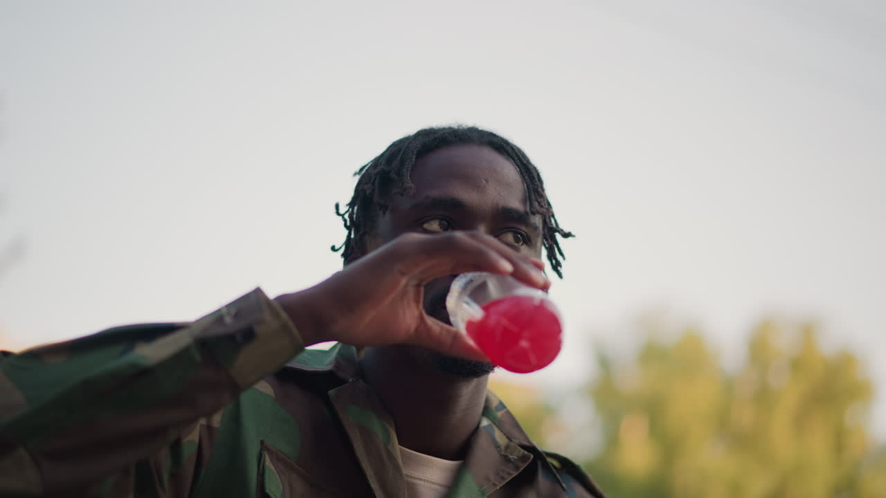 Army Soldier Enjoying Meal Outdoors Peacefully, Military Service Member Resting And Eating During Outdoor Pause, Personnel In Uniform Relaxing And Consuming Refreshments In Open Outdoor Setting