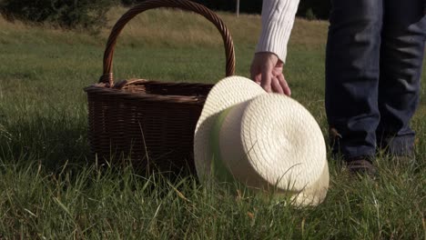 woman putting straw hat and woven basket in a field