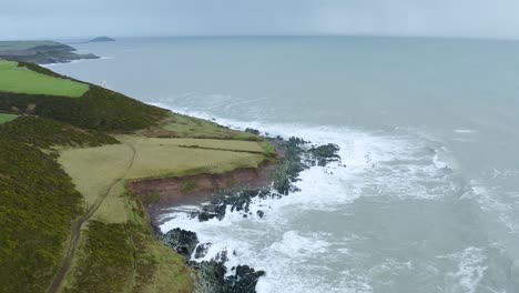 Aerial-drone-shot-of-green-hills-and-ocean-on-Ireland's-south-coast-on-an-overcast-day