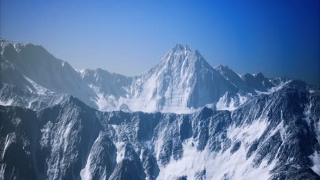 majestic snow covered mountain peak rises above rugged landscape in clear sky