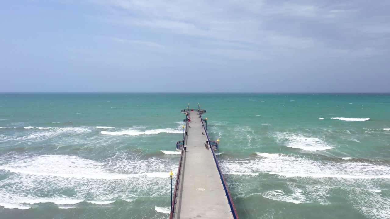 Drone shot flying over length of pier towards open ocean.