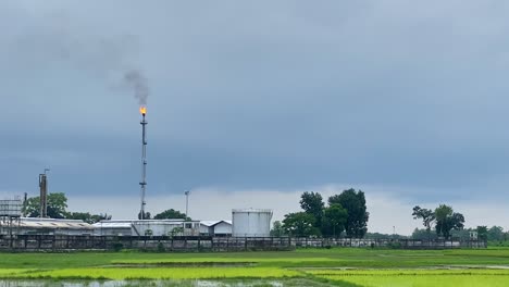 una chimenea arroja fuego y humo en una planta de gas rodeada de un campo inundado