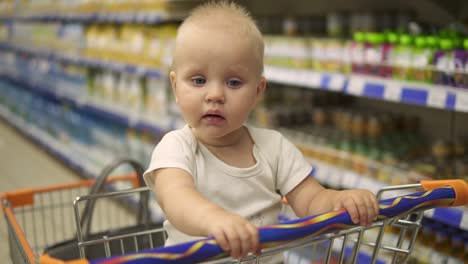 little baby sitting in a grocery cart in a supermarket, while her mother is choosing products. family shopping with a little