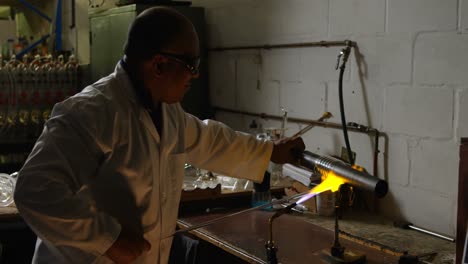 Side-view-of-mature-male-worker-blowing-glass-in-glass-factory-4k