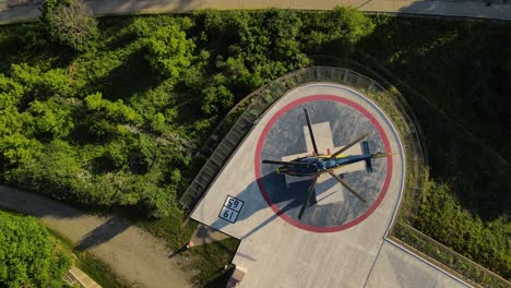 Helicopter-landed-on-pad-near-hospital-building,-aerial-top-down-ascend-view