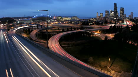 a medida que la hora dorada se oscurece en la noche, el tráfico acelerado en la autopista de seattle se desdibuja en rayos de luz ante el horizonte de una ciudad iluminada