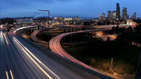 as the goldenhour darkens into night accelerated traffic on the seattle freeway blurs into streaks of light before an illuminated city skyline