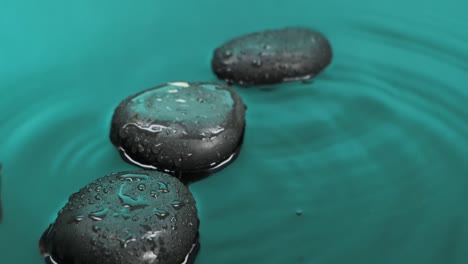 drop falling in green water against a background of calm water and black stones.