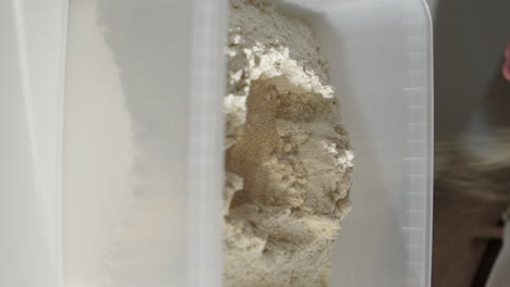 pouring dry yeast in a plastic container with flour making bread dough at home