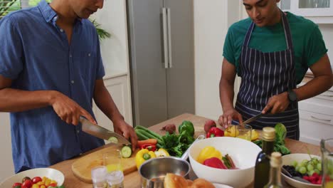 Happy-mixed-race-gay-male-couple-talking-and-preparing-food-in-kitchen