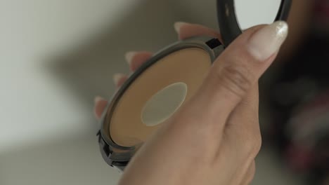 female hand holding foundation with a mirror