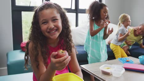 video de una chica biracial feliz sentada con amigos en la sala común de la escuela y comiendo