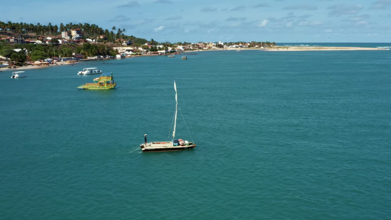 브라질 리오 그란데 도 노르테에 있는 바라 두 쿤하우 해변에서 레스팅가 해변까지 큰 열대 청록색 강에서 항해하는 작은 범선을 따라 공중 드론 샷