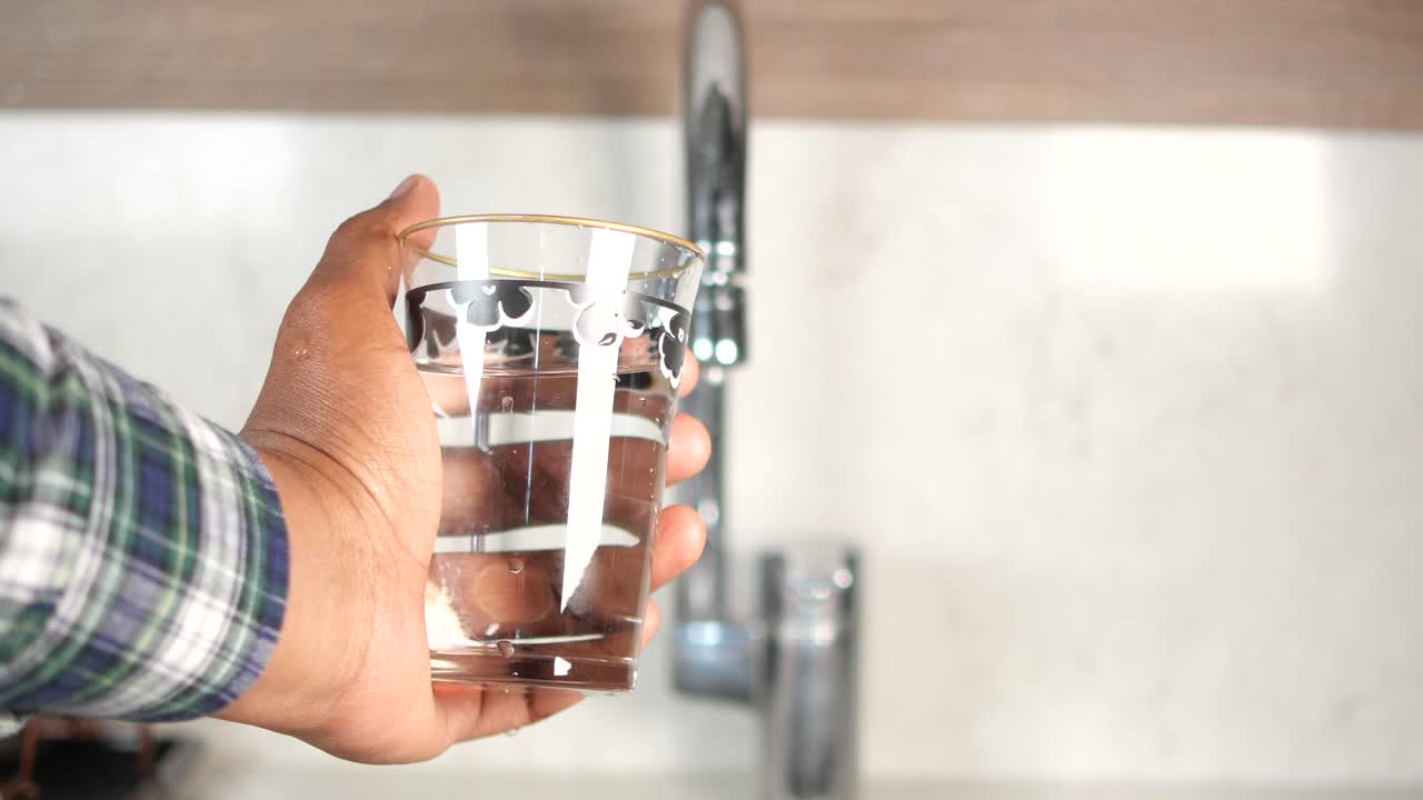 una persona sosteniendo un vaso de agua en una cocina