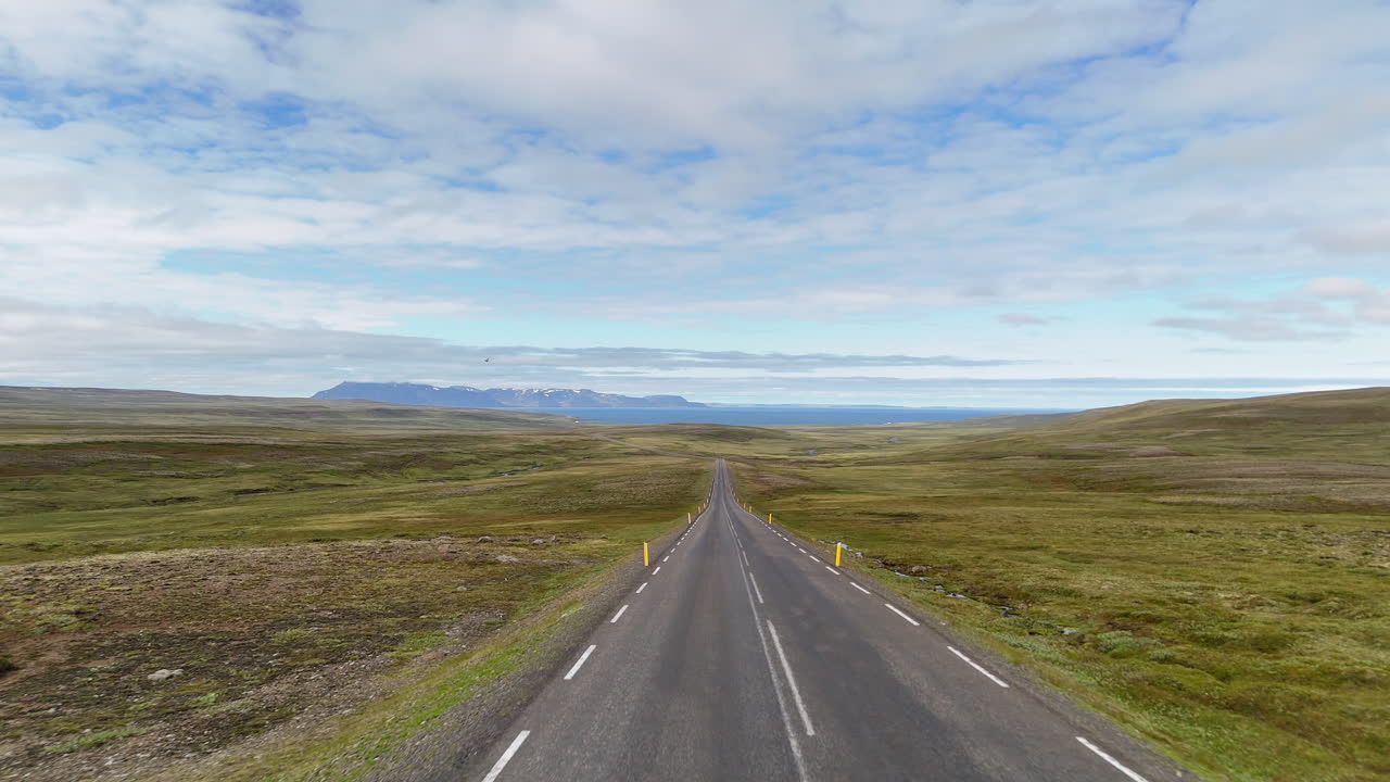 Aerial view of two cyclists riding along Road 1 in the Austurland highlands near Vopnafjörður, crossing open tundra terrain with distant mountains and wide Icelandic skies