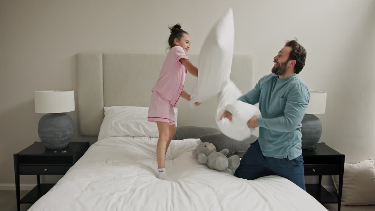 Padre e figlia che fanno una lotta con i cuscini in camera da letto