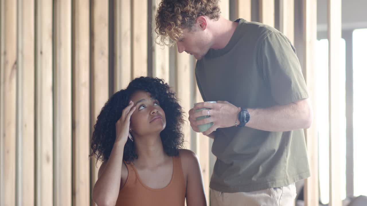 Coppia, con una donna afroamericana che legge documenti al tavolo e un uomo che si china tenendo una tazza verde, mentre controlla.