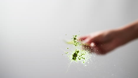 close-up of a hand sprinkling green glitter, freeze-frame effect on a light background