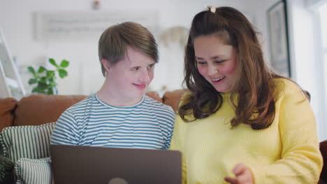 Young-Downs-Syndrome-Couple-Sitting-On-Sofa-Using-Laptop-At-Home