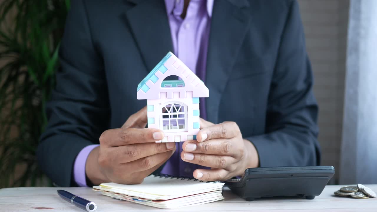 hombre sosteniendo un modelo de casa pequeña en un entorno de oficina