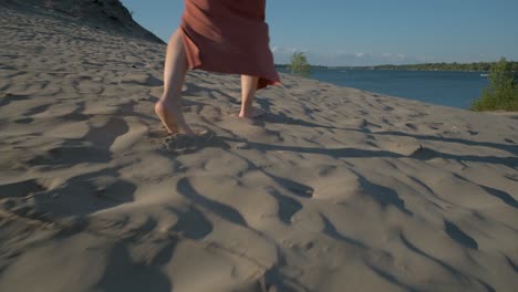 woman walking barefoot in the sand towards the beautiful lake